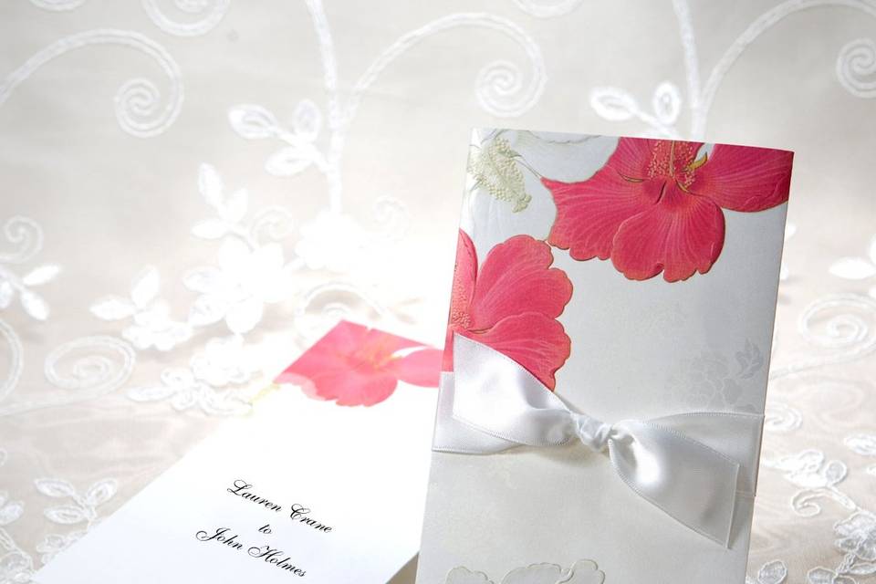 This gorgeous two-part invitation features an outer sleeve and an inner tri-fold insert. On the outer sleeve, beautiful red and white embossed hibiscus flowers lay over a shimmer patterned background. These same hibiscus flowers are flat-printed as part of the tri-fold custom printable insert. The outer sleeve is open at the top for the tri-fold insert, and is accented by a white ribbon and bow.Dimensions: Pocket - 4.5