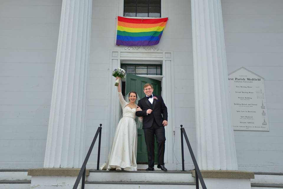 Newly married couple walking out of the church and onto the front steps