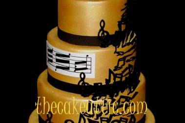 Music themed cake covered in fondant and painted in edible gold luster dust. Piano bottom tier and musical notes dancing their way up the cake. Sugar monogram made to look like sheet music.