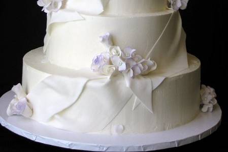 Buttercream cake with fondant drapes and white sugar roses and hydrangeas edged in lavender.