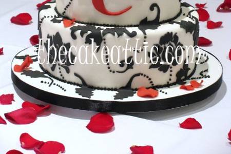 Fondant cake with hand-cut damask design and monogram. Red sugar roses and petals.