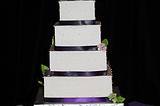 Four tiered wedding cake.   Buttercream icing with satin ribbon border.  Handmade gumpaste flowers by me as the cake topper with gumpaste flowers for decorations around sides.