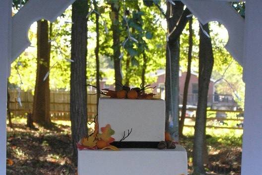 Fall theme three tier square wedding cake with buttercream icing.  Fall decorations of pumpkins, leaves and twigs are handmade from gumpaste.