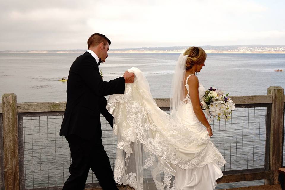 Walking along the Cannery Row boardwalk at the Intercontinental Hotel, Monterey, California, the groom assists the bride with her very long dress!