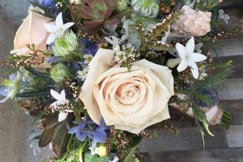 A bouquet of small, delicate textures enhance the sandy colored roses.  Sea shell accents lend to the theme.