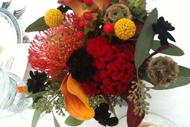 Contrasting colors and textures add visual interest to this Autumn centerpiece of formal and garden blooms, pods and berries.