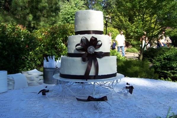 3 tier White Almond Cake with Raspberry mousse filling. Iced in Summer buttercream, accented with picot dots, brown satin ribbon & sparkle centered bow.