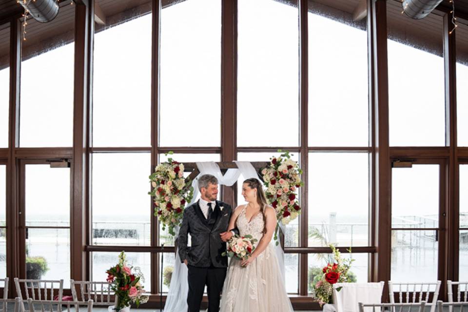 Ceremony at Pavilion at Sunken Meadow, NY – the couple shares a magical moment at the altar, framed by dramatic floor-to-ceiling windows.