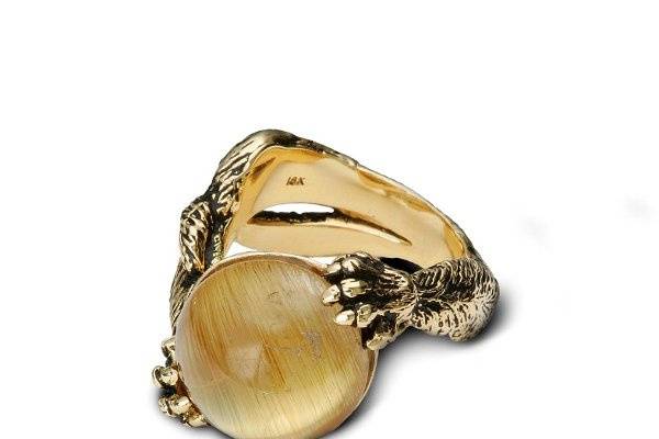 A fun piece that shows a kitty kat at play. The golden quartz resembles a cat’s eye and also a yarn ball, which the cat playfully has in its grip. The ring’s band (shank) is the arms of the cat at its playful pose and tail wrapped along its arm. This ring was designed to fit extremely comfortable around the finger.
Set in 18K Yellow Gold with blackened finish to bring out the kitty’s fur.
Rutiled Quartz. (A golden color cabochon with a cat eye feature). All golden rutiled quartz is natural and will be slightly different in needles/inclusions within the stone.
Carat Weight/Size: 10.87 ct Width of stone is a little more then ½” (14.25mm)