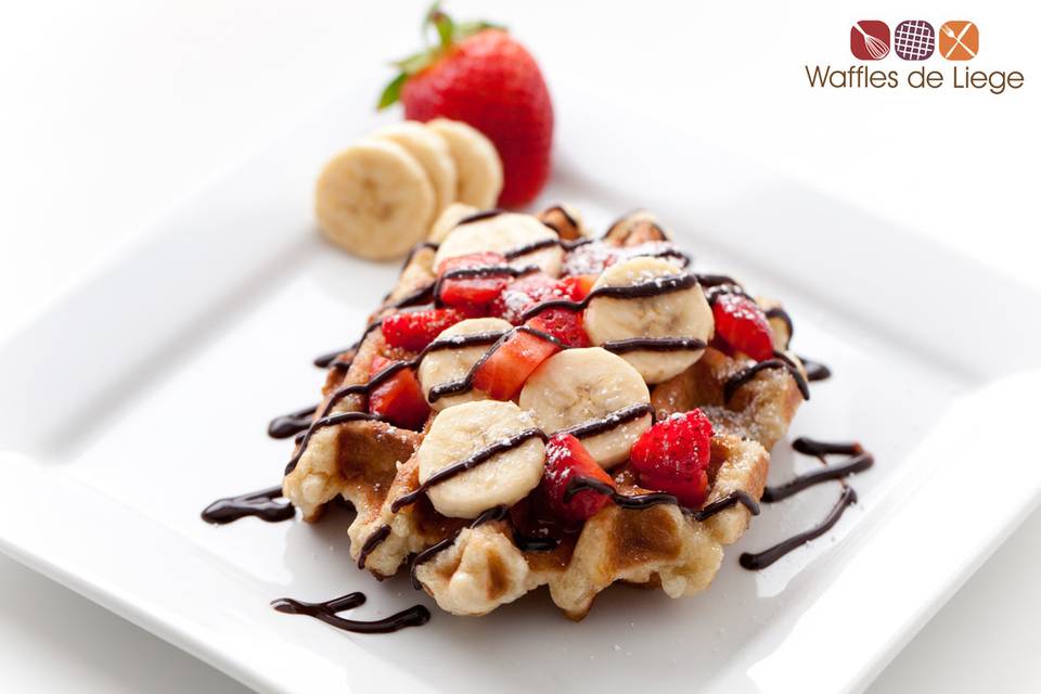 Our Fresh Fruit Waffle features our signature Liege waffle with fresh strawberries, bananas, and chocolate syrup. Additional toppings like whipped cream and sliced almonds are also available.