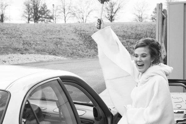 A bride throws her hand up in a victorious goodbye as she climbs in the car to drive off into the sunset with her new groom.