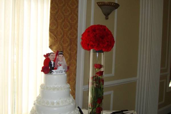 High centerpieces designed with a ball of red carnations atop a clear glass cylinder filled with a spiral of red roses by Stein Your Florist Co. A couple of red roses accent the cake as well.