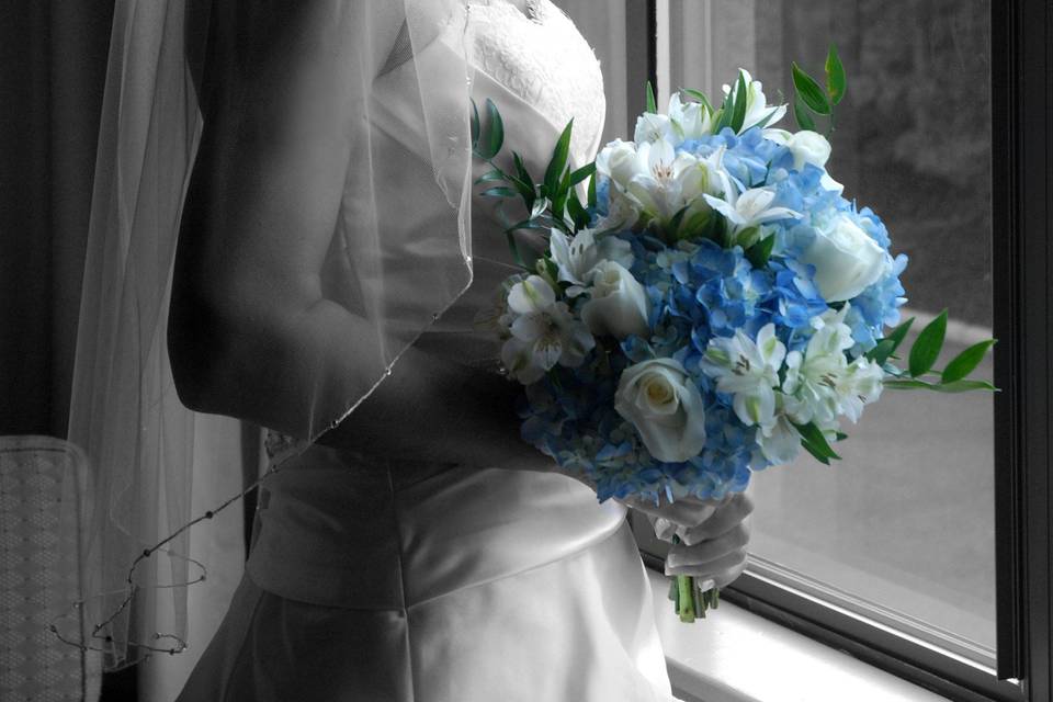 Bride looking out window in black and white with spot color of blue flowers.