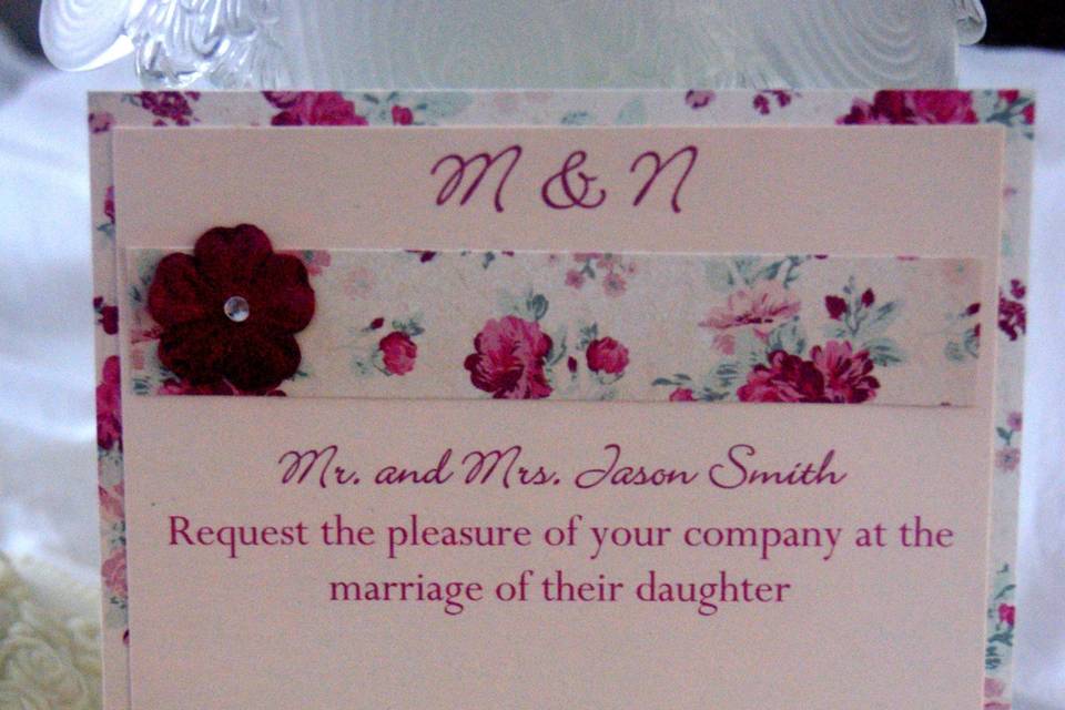 Romantic rose wedding invitation is printed on pale pink pearl card stock and layered with rose card stock and rose border across the top. Top border is embellished with rose and rhinestone.