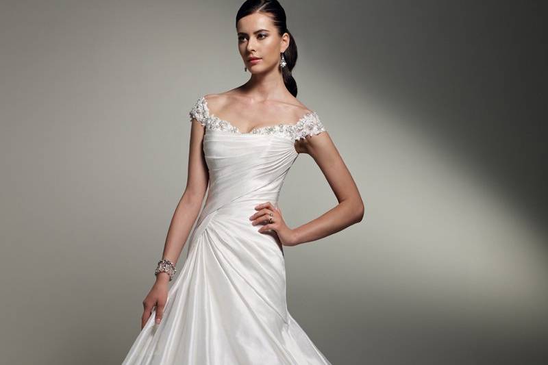 Y21243 - Rosemary <br>
Paint the prefect bridal picture in Rosemary, a demure yet dazzling ball gown in Marseille taffeta. Lace appliqués hand-beaded with crystals adorn the unique off-the-shoulder neckline. A superbly draped bodice is perfectly balanced by the grand skirt with pick-up detail, featuring rosettes and lace appliqués. A flourishing bustle in the chapel length train and a functional corset back complete this lovely gown.