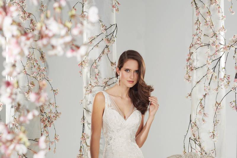 Style #y11400<br>
Margaery boasts timeless elegance in misty tulle and lace. Delicate tulle shoulder straps frame the V-neck décolletage, softening the sweetheart bodice. Tulle is richly draped through the asymmetrically dropped waist bodice of the modified mermaid silhouette, complemented with scattered crystal hand-beaded lace appliqués. A sensual deep V-back bodice is finished with a concealed back zipper featuring diamante buttons while the scalloped lace chapel length train completes the look.