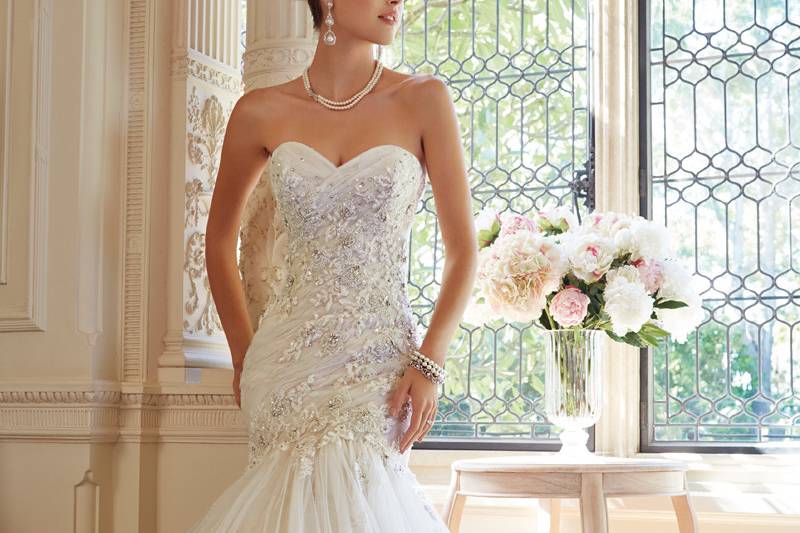 Y21449 - Marsha<br>
2014 Collection – A slimming draped bodice accented with dainty lace appliqués will enhance your figure in this modified mermaid opal organza gown. Marsha features a strapless illusion scooped neckline trimmed with scalloped lace and an asymmetrically draped bodice with lightly hand-beaded lace appliqués that cascade down the flared skirt with a chapel length train. A back corset finishes off this charming gown.