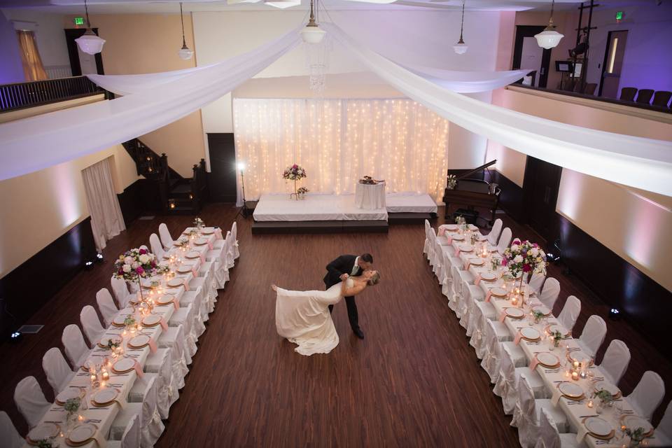 The Main Ballroom is a wonderful, large gathering space. Perfect for wedding Ceremonies, Receptions, Galas, lectures, presentations, play readings, workshops, and celebrations, this room can fit 125 for a cocktail reception or 100 seated guests (chairs and tables in picture shown). The room measures 39' X 39' and has 6 different entrances and exits. This marvelous hall features a wrap around balcony along three sides, a stage, a baby grand piano, and a projection wall (high-quality Epson projector available to rent for an additional fee).Located on our main floor, this room is completely ADA-accessible and ready for your event.