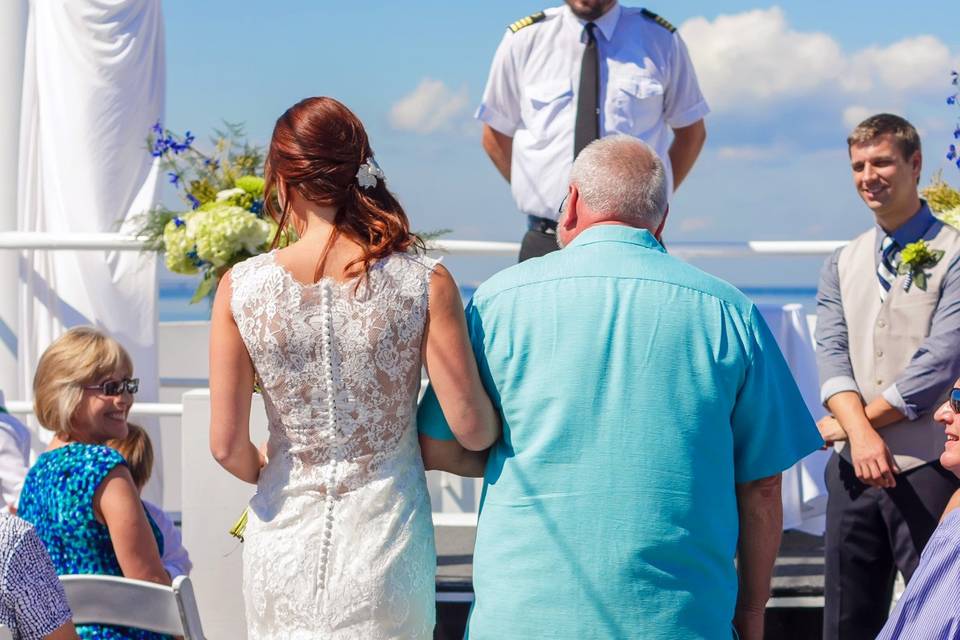 The bride and dad walking down the aisle of the sky deck on the SOLARIS yacht.