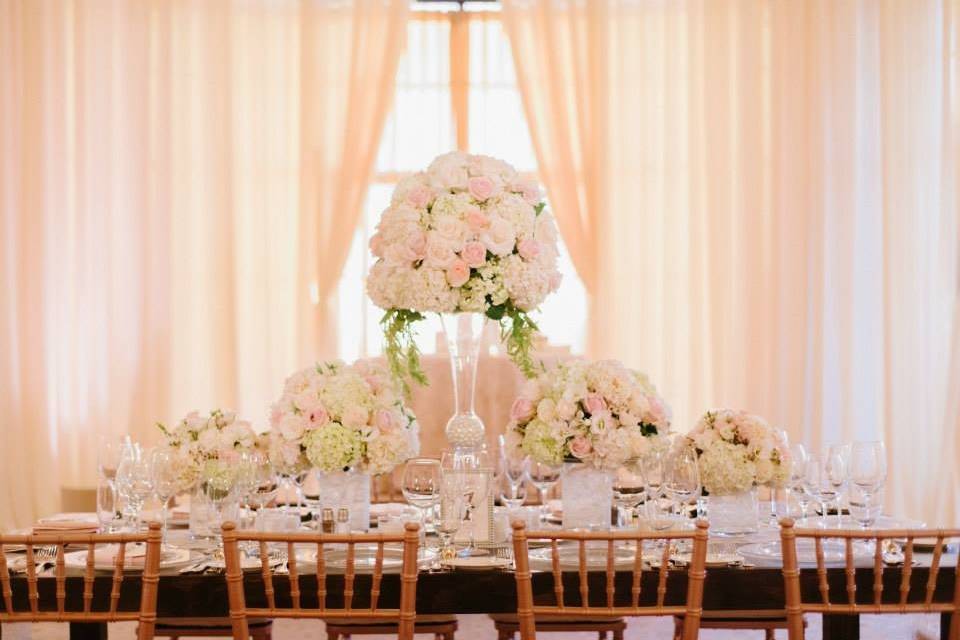 Lush and bright tablescape with centerpieces of differing heights. Designed with blush and white hydrangea and blush roses with complimentary accents.