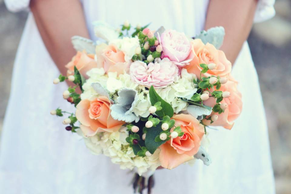 Bridesmaid bouquet designed with white hydrangea, peach roses, pink garden spray roses, white hypericum and dusty miller.
