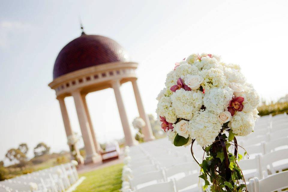 Lush garden styled arrangement designed with white hydrangea, cream roses and pink cymbidium orchids with trailing ivory over wrought iron stand at the beautiful Pelican Hill Resort.