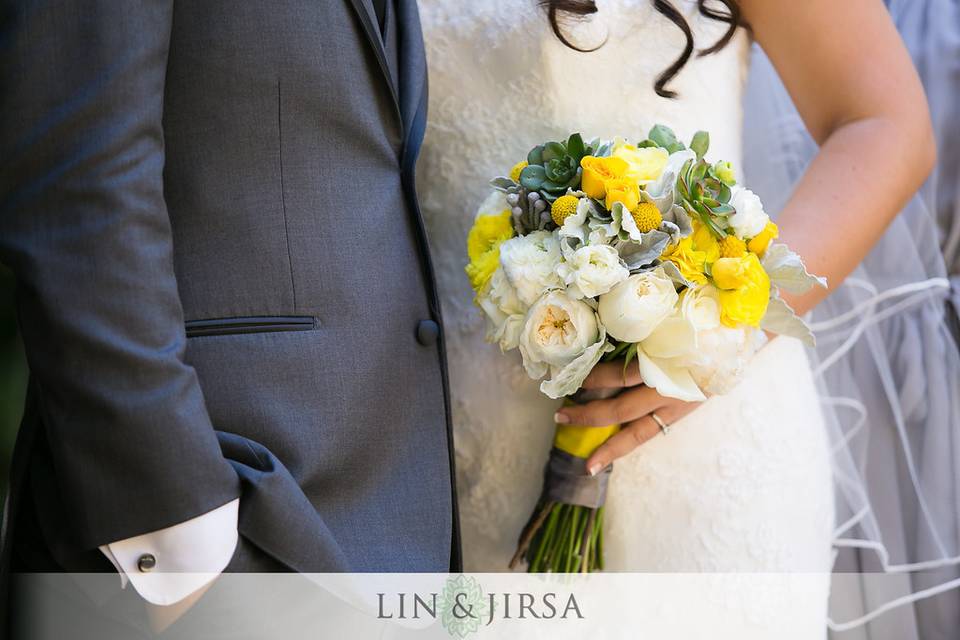 Playful and bright bridal bouquet designed with white garden roses, white and yellow ranunculus, yellow billy balls, yellow spray roses, succulents and dusty miller, perfect for this garden wedding.