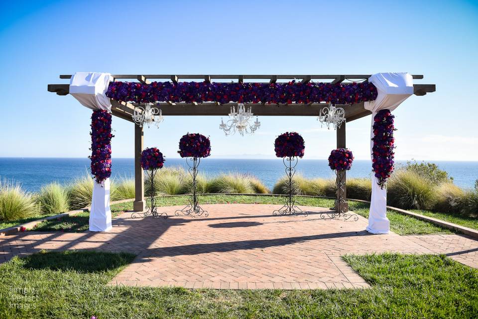 Beautiful wooden arbor overlooking the coast at Terranea Resort.  Front and side pieces designed with purple hydrangea, purple lisianthus and fuchsia roses.