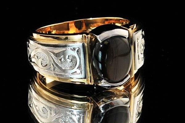 Gentleman's Black Star Sapphire set in 18k white and yellow gold.  The client chose the Sapphire for a number of reasons, for durability and beauty.  18k gold white shoulders are hand engraved.
This design is suitable for an oval, cushion or round center gemstone.  Please see the Blue Sapphire example also featured in our album.