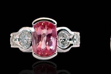 A variation of the ring featuring the Champagne Diamond (listed herein) we used a oval cut Pink Sapphire for the center and two round Diamonds on each side.  The setting was modified to allow the placement of burnished 