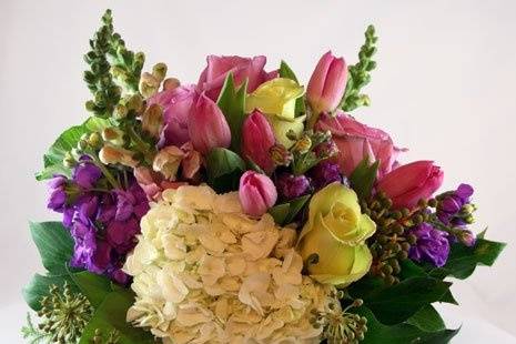 Floral arrangement designed in glass vases lined with decorative green leaf.  Hydrangeas, roses, tulips, etc. were used in the arrangement.