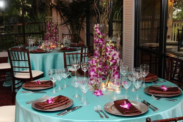 Three different size cylinder vases with purple dendrobium orchids and curly willow branches under water.  Dendrobium orchid bloom on each napkin.  Flowers were for a TV commercial for Celebration Events Window on the Waterway.