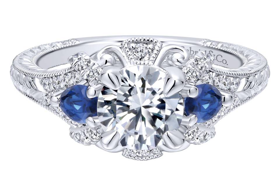 ER12582R4W44SA	<br>	This antique-style engagement ring's grand halo boasts a pair of sapphire side stones in addition to diamonds and romantic white gold flourishes. A band with engraved details and milgrain borders enhances the ring's vintage appeal