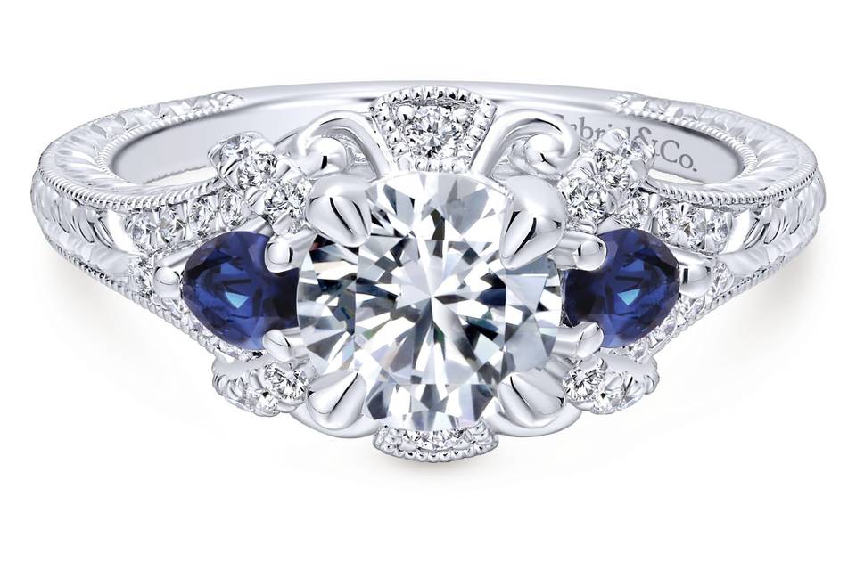 ER12582R4W44SA	This antique-style engagement ring's grand halo boasts a pair of sapphire side stones in addition to diamonds and romantic white gold flourishes. A band with engraved details and milgrain borders enhances the ring's vintage appeal.