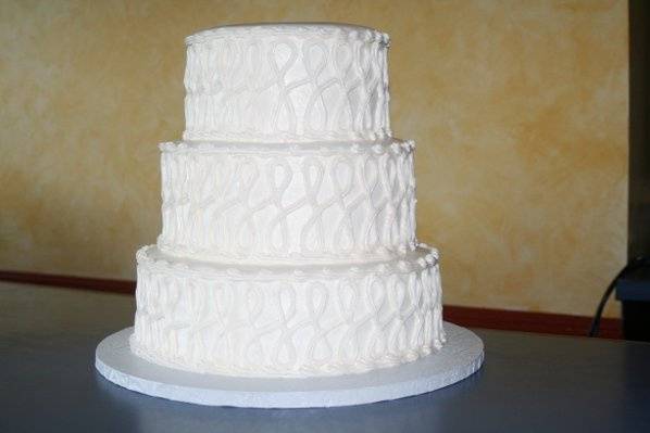 Three tiered cake with buttercream frosting and white-on-white figure 8 design