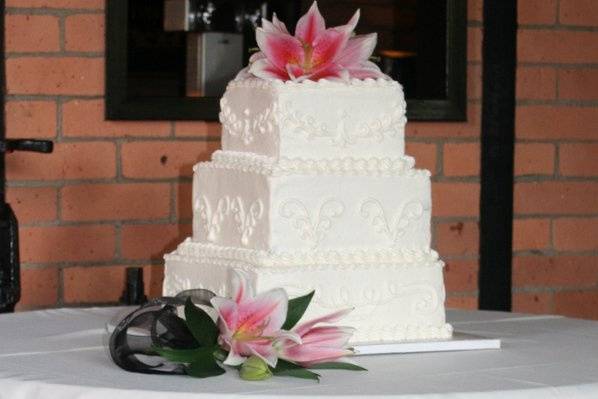 Three tiered square cake with scroll design on the sides and fresh flowers