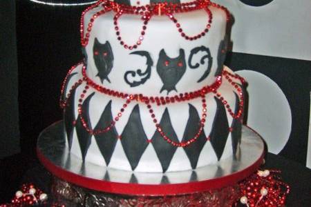 Styled in the Goth style, this cake features two owls, in love with each other atop the harlequin topsy turvy cake. Red beads accent.