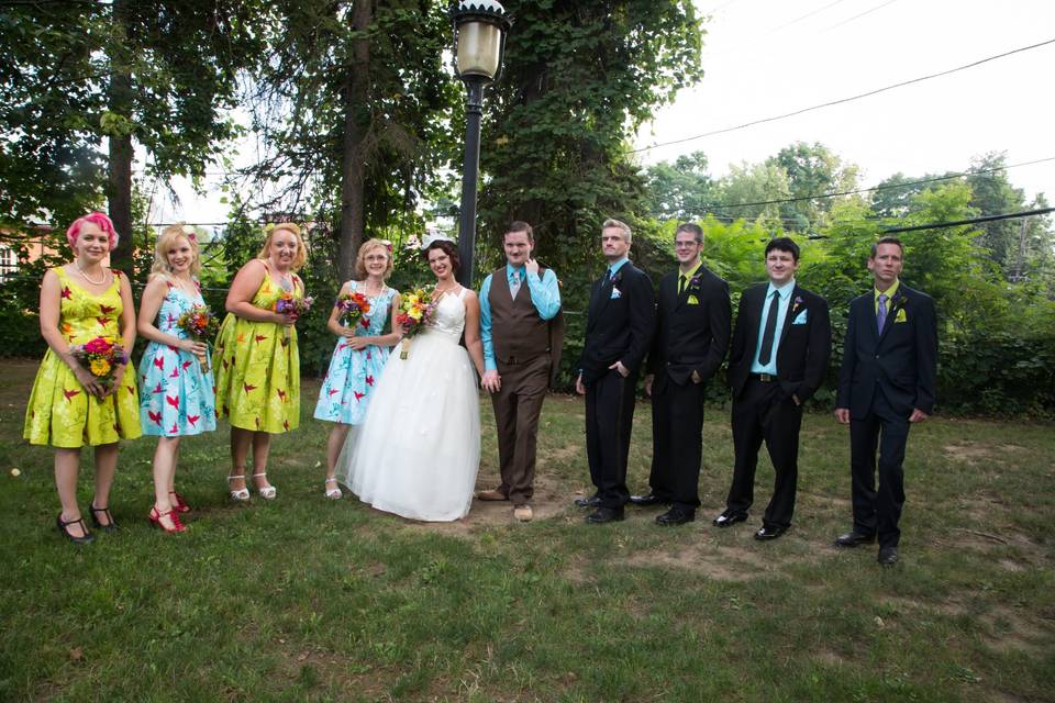Here is the complete bridal party with the brides maids in colorful cotton print dresses and the bride in silk art deco style bodice with tulle skirt dotted with roses to match train.