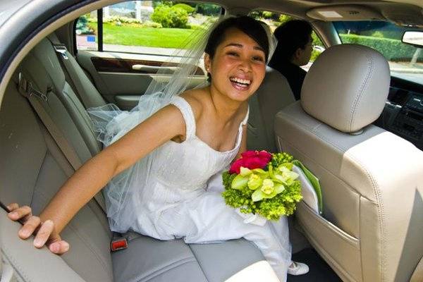 Waiting to come in for her wedding the bride sits in the car with her flowers. Boston, MA