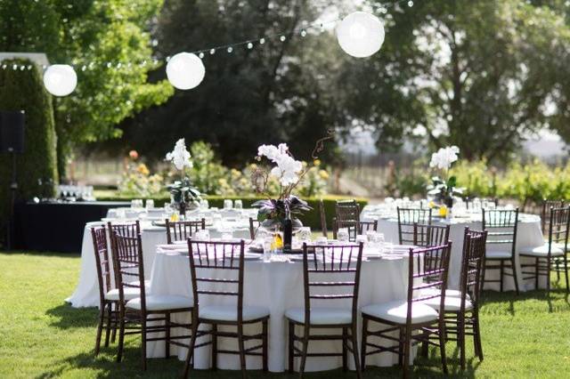 Dark Brown Wood Chivari chairs, ivory lanterns, bistro lights, wine barrel tops with orchid centerpieces and ivory linen.