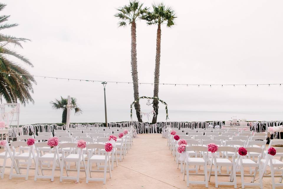 The Ceremony chairs were adorned with bright pink hydrangeas and trailing ribbon. The floral alter featured a crystal chandelier framing the Bride and Groom and a pennant flag banner hung between the two palm trees read 