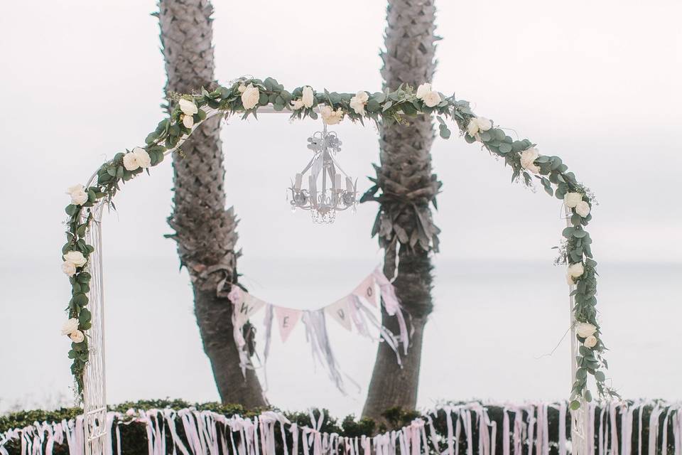 Close up the rose adorned arch with crystal chandelier. Shabby chic wreaths and garlands added to the decor