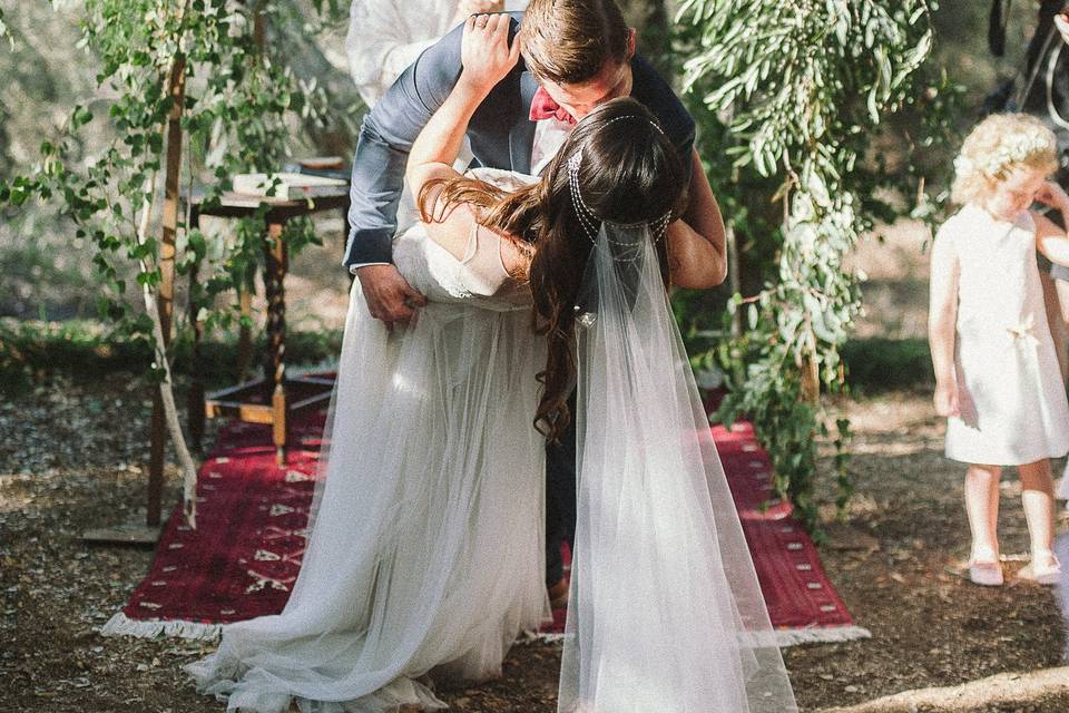 The Ceremony took place in a lower clearing on the working Olive Oil Ranch under the shade of Oak Trees. The site was made special with a natural arch and gorgeous floral and greenery by Adornments and a beautiful red rug tied everything together perfectly.