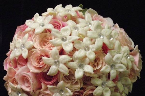 Light orange and ivory roses mixed with astible and adorned with rhinestones in a hand tied bouquet.