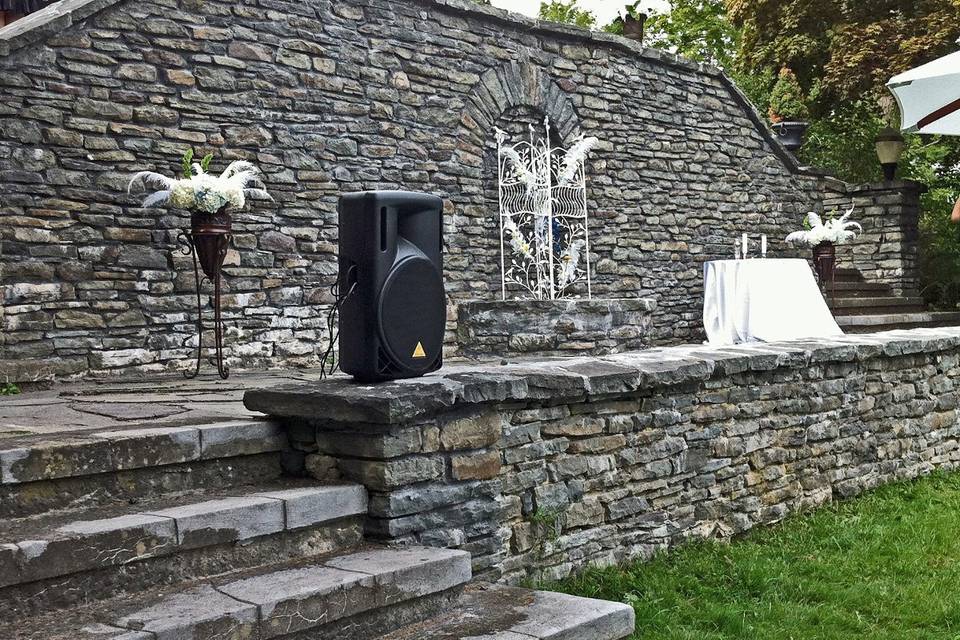 The fieldstone wall atop the upper lawn of The Mansion at Noble Lane in Bethany, PA is the setting for the nuptials of Marcus and Nicola.  Plumed urns of Hydrangeas and a white wrought iron screen adorned with feathers and flowers set the stage.