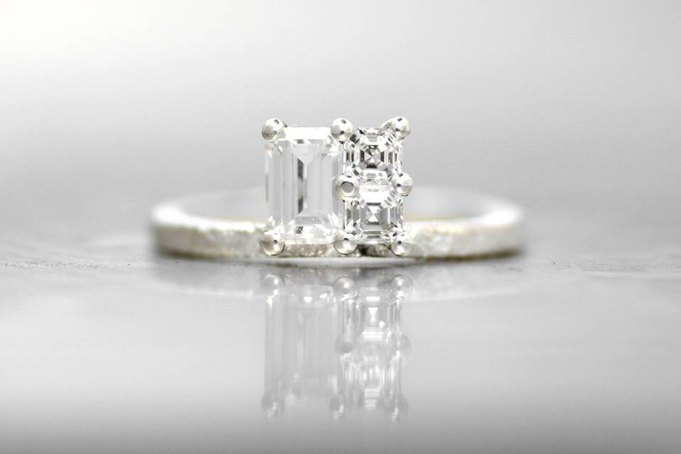 GENEVAThis simple offset cluster gives the allure of a single large square diamond in this stunning engagement ring. The emerald cut white diamond and two asscher white diamonds elongate by climbing up or down the finger. The signature Wanderlust textured band creates a subtle and organic feel that will wear perfectly over time.