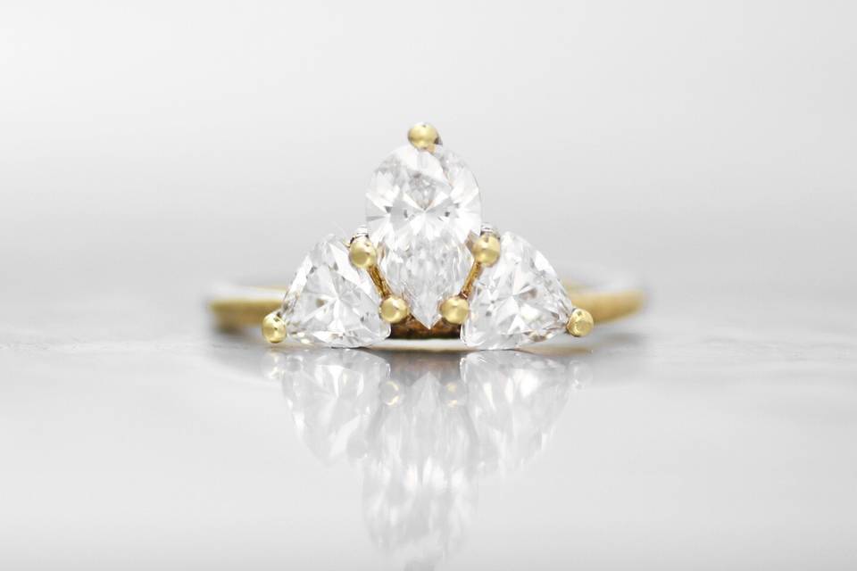 VERSAILLESA unique combination of diamond shapes in a clustered prong setting, this engagement ring delicately sits on the finger with elegance and sophistication. This design features an offset pear shaped white diamond nestled between two trillion white diamonds to create a symmetrical shape that will elongate by climbing up or down your finger. The signature Wanderlust textured band creates a subtle and organic feel that will wear perfectly over time.