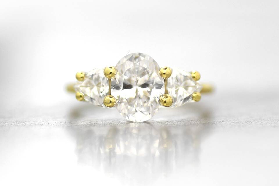 Oval shaped white diamond flanked by two trillion white diamonds in 18k yellow gold textured setting