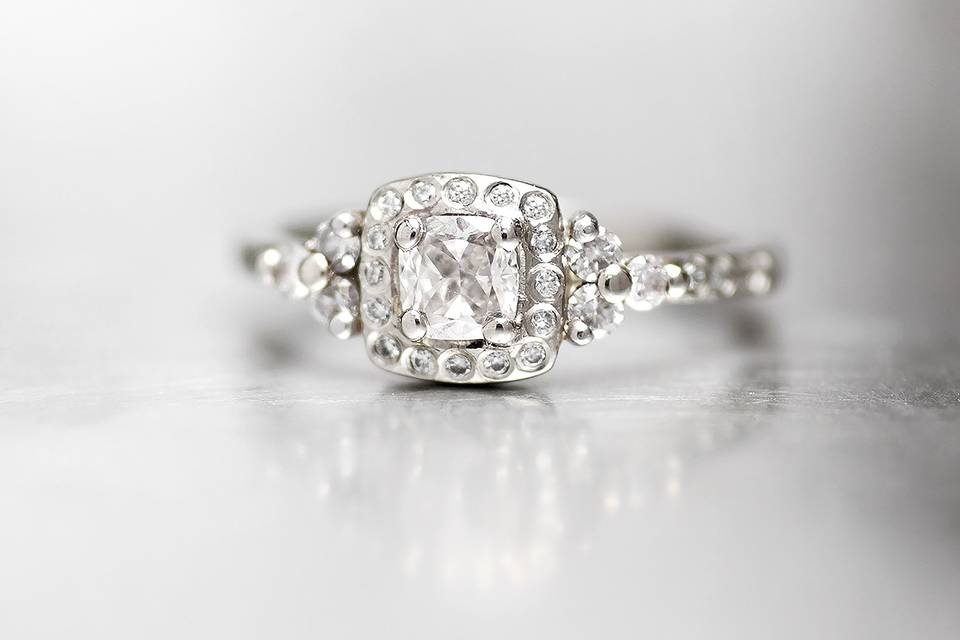 White gold engagement ring with cushion cut center stone and surrounding white diamonds.