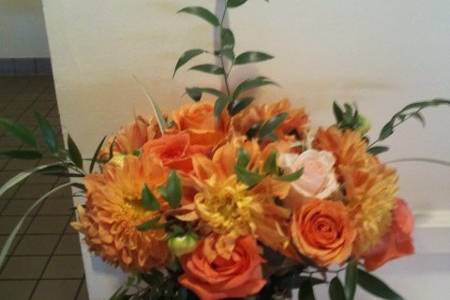 Guest/gift table arrangement. Orange, cream, and red-gold roses, orange dahlias, orange ranunculus, and greens.